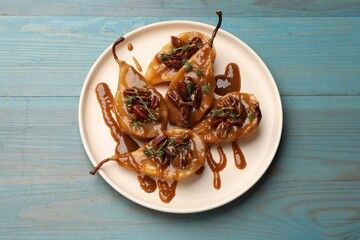 Delicious pears with caramel sauce, pecan nuts and thyme on light blue wooden table, top view