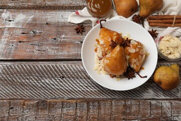 Delicious pears with caramel sauce, almond flakes and spices on wooden table, top view. Space for text