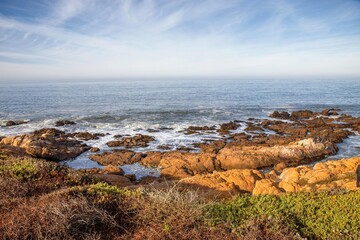 View of the Pacific Ocean at dusk, rocky shore beach, fog in distance, nobody
