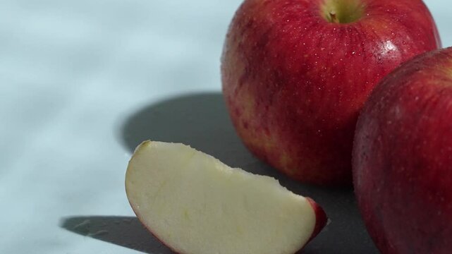 Close up of red apples with a slice on blue wet background. Macro of sliced apple with apple place at blue background and water spilling and waving. Healthy eating and fresh produce concept. Pabulum.