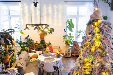 Festive Christmas decor in living room in a green house in the loft style with a retro wooden lampshade with a snowy Christmas tree and fairy lights. New Year, Christmas mood, cozy home.