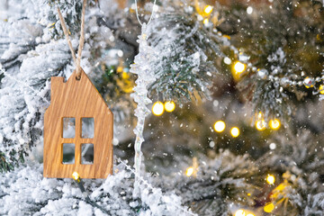 Naklejka premium Key and tiny house keychain in hand on background fairy lights Christmas tree. gift for New Year, Christmas. Building, design, project, moving, insurance, mortgage, rent and purchase real estate.