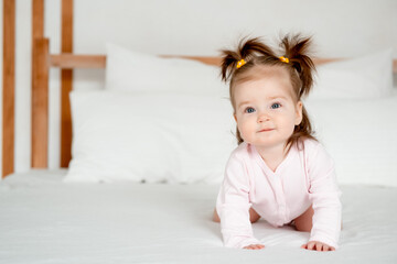 Fototapeta premium Funny baby girl in pink bodysuit on the bed in the bedroom smiling or laughing, cute little baby at home, place for text