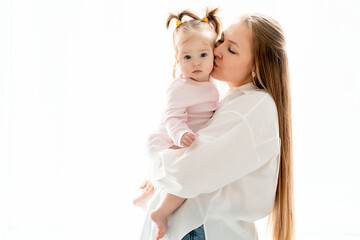 a mother with a baby daughter, a mother gently hugs her baby girl kissing, maternal love and care, a happy family with a baby on a white isolated background, a place for text