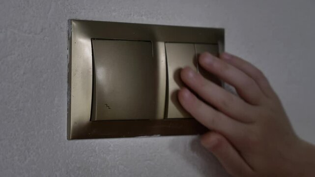 Close-up of a light switch on a wall as a small child's hand reaches to toggle the switch on or off within a home environment