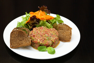 Raw meat tartare for gourmets. Raw meat tartare with spices, croutons and herbs. Beef tartare with capers. Beef tartare with bread slices.