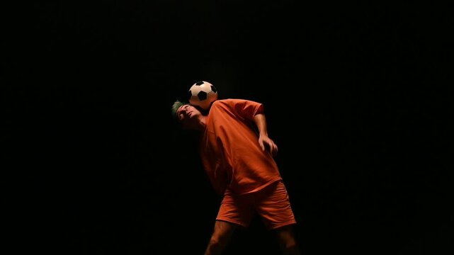 Football freestyle of a guy in an orange uniform on a black background . A football player fills a ball on a black background. A young man juggles a ball. 
