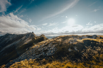 The bright sun is shining beautifully through the clouds above the mountains