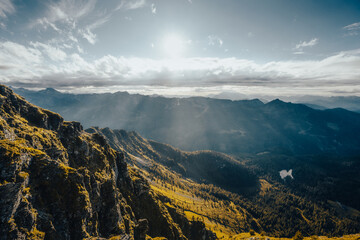 The sun shines brightly through the clouds above the mountains