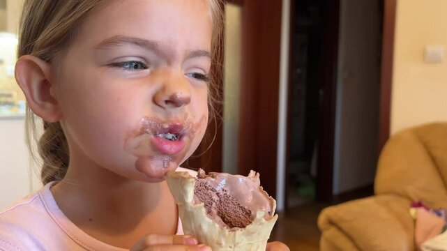A little girl with chocolate smeared on her cheek, nose, and mouth is making a silly face, with a big smile and messy hair