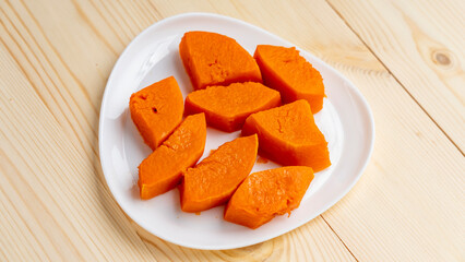 Pieces of baked pumpkin on a white plate on a wooden table. top view, close-up.