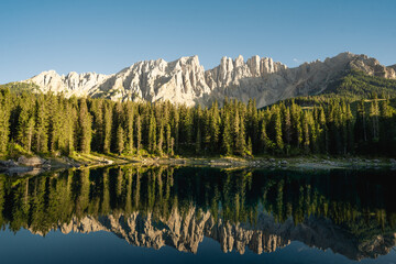 A mountain range reflects in a calm lake, surrounded by lush trees