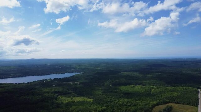 Aerial drone view over the lush Matapedia forest and Lac du Portage under a moody panoramic cloudy sky in Sainte-Paule, Quebec, Canada; high-altitude wilderness landscape.