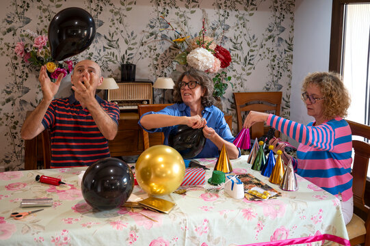 Friends smiling and inflating balloons at a decorated table for a birthday celebration - Powered by Adobe