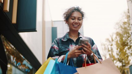 Young woman using smartphone while carrying shopping bag