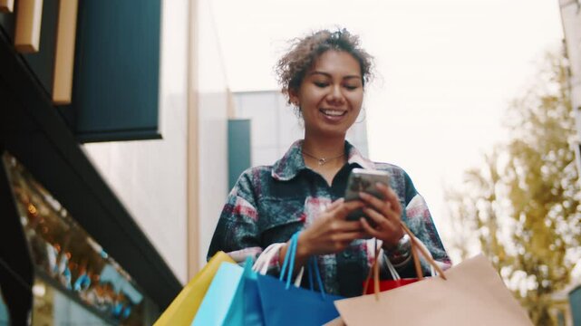 Young woman using smartphone while carrying shopping bag