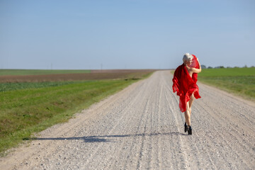 Fototapeta premium Courage and Freedom: A woman posing with a red scarf on a rural road, with a panoramic view of the horizon