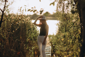 Lady with vibrant red hair, dressed in snug white jeans, stylish black top, and wide-brimmed white...