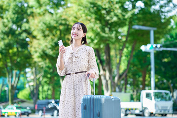 スーツケースとスマートフォンを持って街を歩く若い女性