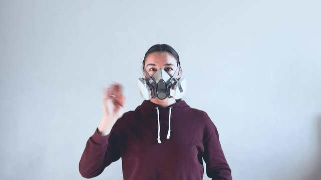 A young attractive girl in a protective gas mask looks at the camera and waves her hand.