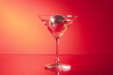 Cocktail party with disco ball on sunset coral color background. Disco party, retro fashion. Modern stylish backdrop template for holiday card, banner, flyer, menu with space for text