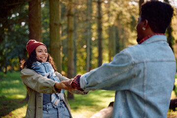 Playful couple having fun while spinning in park in autumn day.