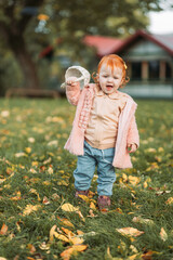 Baby ginger, redhead girl walking outdoors in the park, playing with a basket