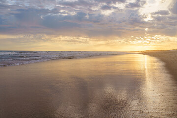 Golden sunset reflecting on a serene, empty beach.