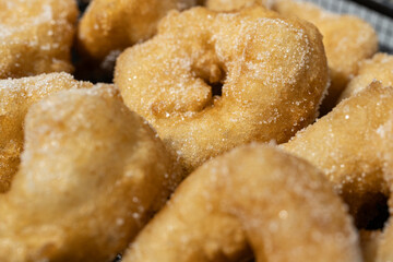 Golden doughnuts sprinkled with sugar cooling on a wire rack. These freshly fried doughnuts are soft on the inside and crisp on the outside, perfect for festive or holiday gatherings.
