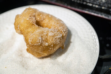 A close-up of a freshly fried doughnut being coated in sugar as part of the preparation process during Hanukkah celebrations. This traditional sweet treat is commonly enjoyed during this holiday.