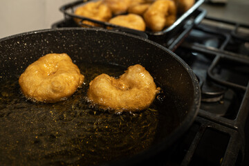 Close-up of golden sufganiyot doughnuts frying in hot oil on a stovetop, a traditional Hanukkah treat. The doughnuts are later sprinkled with sugar, highlighting their crispy texture.