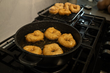 Close-up of golden sufganiyot doughnuts frying in hot oil on a stovetop, a traditional Hanukkah treat. The doughnuts are later sprinkled with sugar, highlighting their crispy texture.