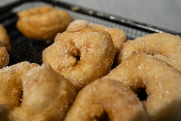 Golden doughnuts sprinkled with sugar cooling on a wire rack. These freshly fried doughnuts are soft on the inside and crisp on the outside, perfect for festive or holiday gatherings.