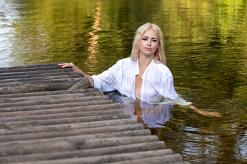 Portrait of a young beautiful blonde girl in a white shirt near the river.