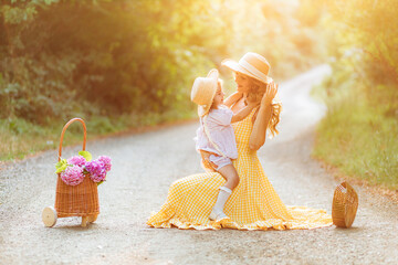 Young mother in a beautiful yellow dress holding her daughter. Country road