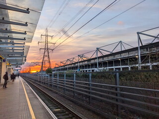 London - 03.14.2024: Passengers waiting for a train at the Custom House Elizabeth Line station behind the yellow line next to the Excel Exhibition Centre during sunrise with the sun at the horizon