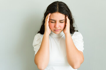 Teenage girl in distress, holding her temples and closing her eyes due to a severe migraine