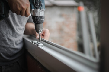 Caucasian man installs fittings for a window frame with a drill.