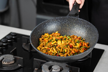Close up of Chef cook hands cooking and toss roasted pasta, onion, pepper, carrot, vegetables, mushrooms, green peas, beans, garlic in frying wok pan on gas stove. Flying food levitation.