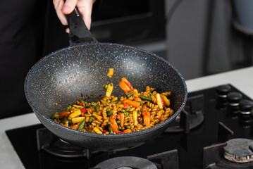 Close up of Chef cook hands cooking and toss roasted pasta, onion, pepper, carrot, vegetables, mushrooms, green peas, beans, garlic in frying wok pan on gas stove. Flying food levitation.