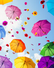 Obraz premium Colorful umbrellas float against a blue sky with falling flowers