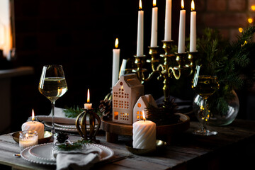 Elegant decor for Christmas family dinner. Center piece with burning candles, vintage chandelier. Zero waste eco-friendly reusable home decoration, fir tree branches. Cozy atmosphere, wooden furniture