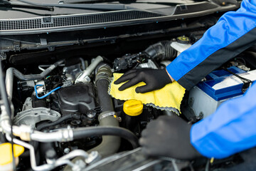 A mechanic performing maintenance on a car engine using a cleaning cloth in an automotive repair shop during the afternoon