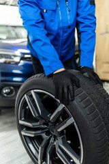 A mechanic in a blue jacket changes a car tire in a well-lit garage during the day with a focus on the process and tools used