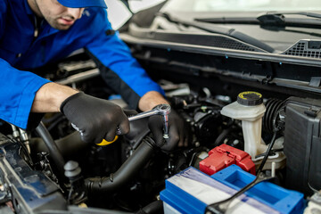 Mechanic performs maintenance on a car engine in a workshop during daylight hours