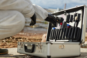 Close up of unrecognizable scientist wearing hazmat suit and using toolkit case while taking probes outdoors, copy space