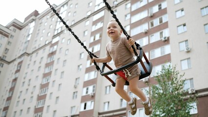 Happy child swinging high having fun at playground in residential area