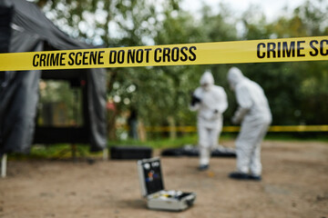 Background image of crime scene with yellow Do not cross tape and blurred shapes of people working,...