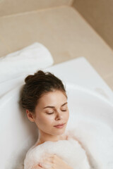 Serene young woman relaxing in a bubble bath, eyes closed and enjoying self-care in a modern bathroom. Wellness and relaxation concept.