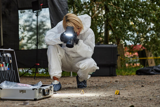Full length shot of female forensic investigator working on crime scene and taking photos of evidence, copy space